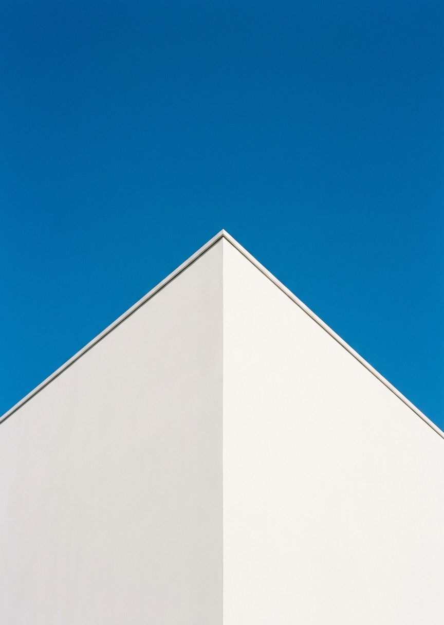 Minimalistiskt arkitekturfoto av en vit modern byggnad med rena geometriska linjer mot en klarblå himmel.