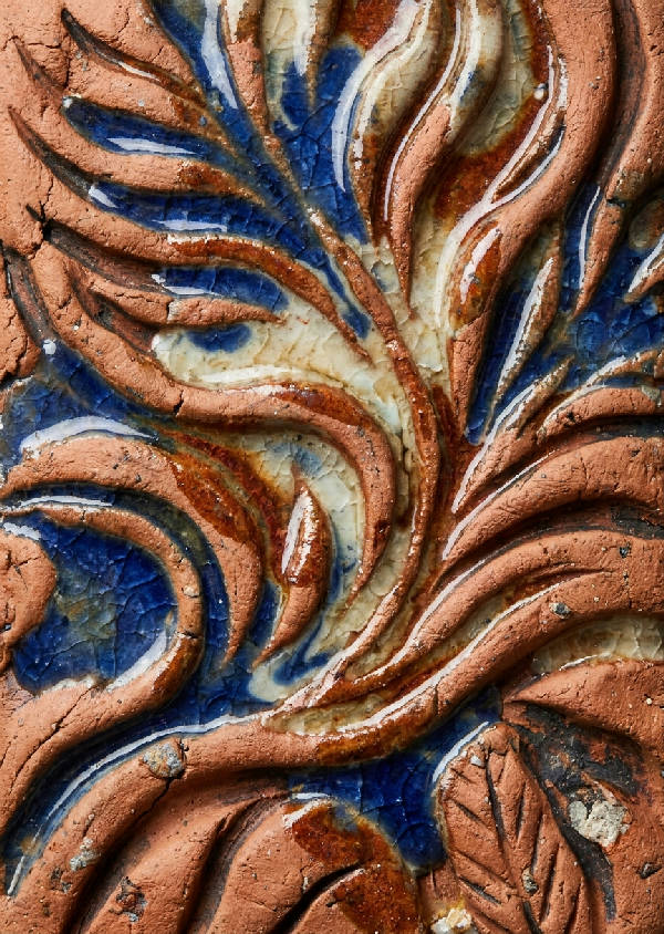 Makrofotografi av en handgjord keramisk platta med en intrikat mönstring av vågor och blad i relief.