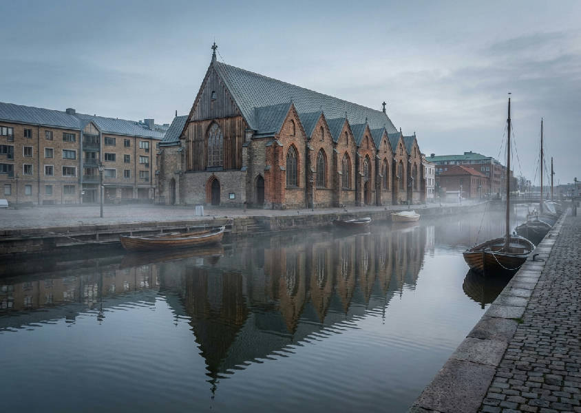 Feskekôrkan i Göteborg reflekteras i det lugna kanalvattnet under en molnig himmel, arkitekturfokus.