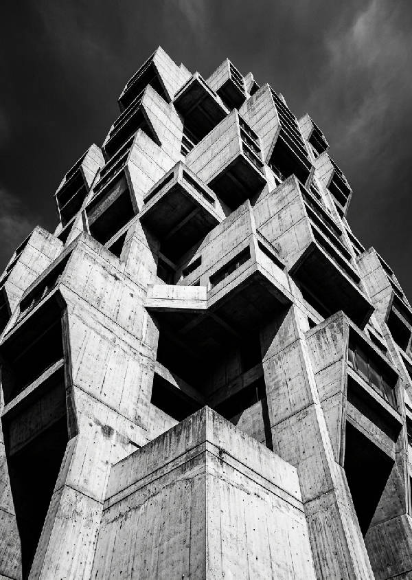 Vertikal bild av en massiv brutalistisk betongbyggnad med skarpa geometriska linjer och djupa skuggor. Ett arkitektoniskt fotografi i monokrom stil som framhäver strukturen.