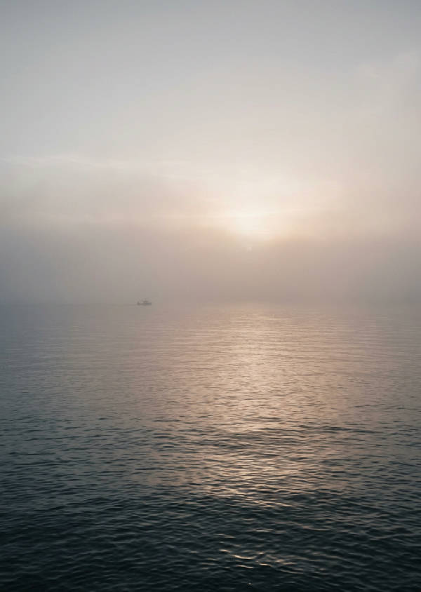 Vertikal bild av ett dimhöljt hav med minimalistiska gråa nyanser som skapar en lugn atmosfär.