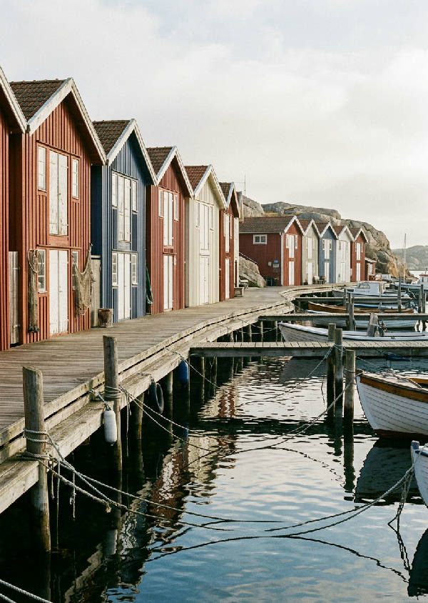 Mjukt fokus 35mm filmfotografi av färgglada båthus längs Smögenbryggan, sett från vattnet med reflektioner och morgonljus.