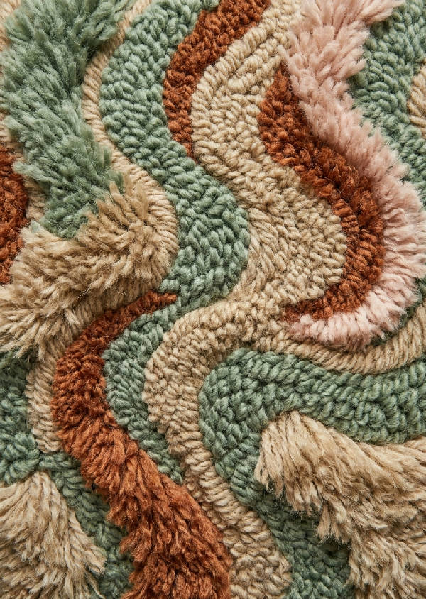 Makrofotografi av en tuftad ullvävnad med vågiga, abstrakta former i mjukt grön, beige och rosa. Detaljerade fibrer skapar en 3D-effekt.