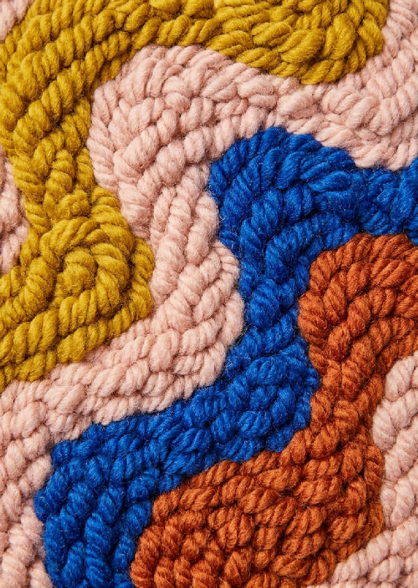 Makrofotografi av tuftad ulltextil med vågiga mönster i senapsgul, rosa, koboltblå och roströd.