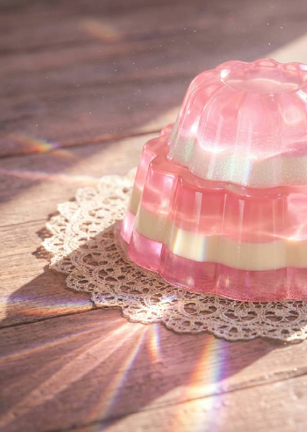 Makrofotografi av en skiktad, genomskinlig rosa gelédessert på en vintage virkad duk med ljusmönster
