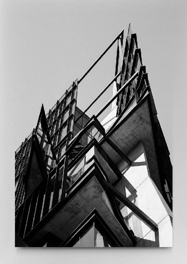 Svartvit abstrakt fotografi av en byggnad med skarpa linjer och geometriska former, sedd underifrån. Kontrastrik bild med djupa skuggor och ljusa ytor.