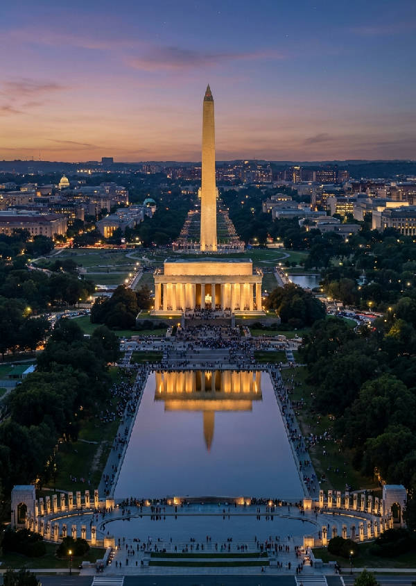 Flygfoto över Lincoln Memorial vid skymning, med spegelbild i Reflecting Pool och Washington Monument i fjärran, i lila och orange himmelsljus.