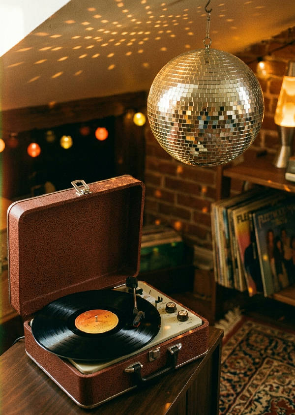 Närbild på en vintage skivspelare med en reflekterande discokula i bakgrunden, allt i en lila nyans