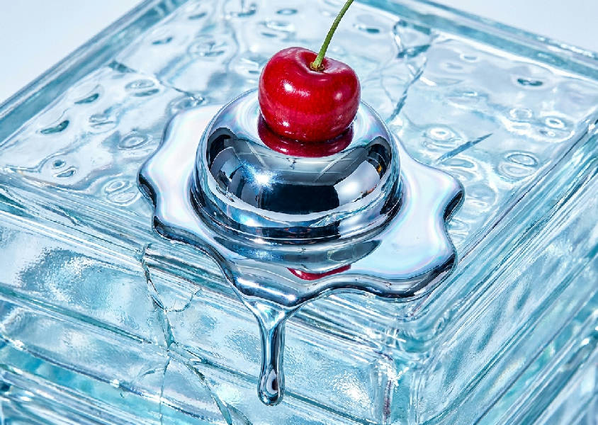 Ett makrofotografi av en smältande kromsfär med ett rött körsbär på ett genomskinligt glasblock. Den har en Y2K-futuristisk estetik.