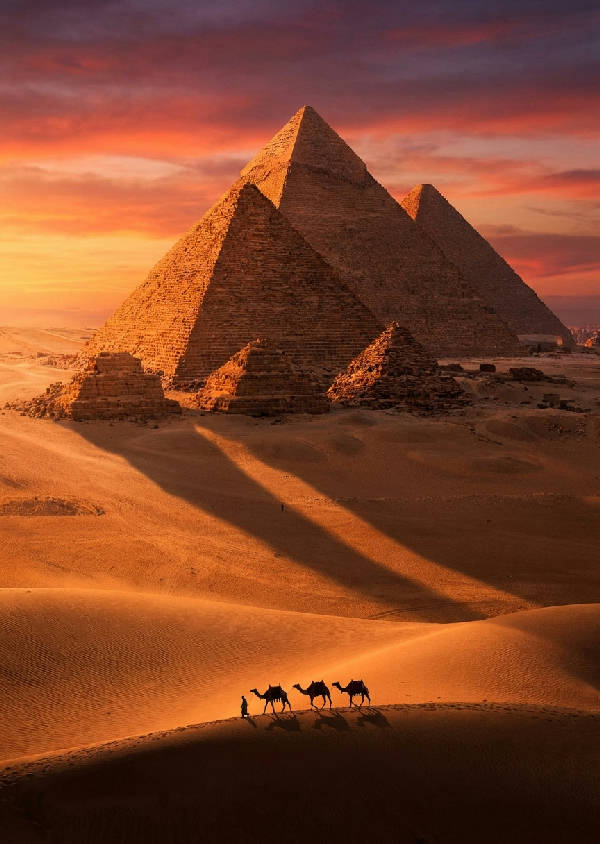 Hyperrealistiskt fotografi av pyramiderna i Giza i solnedgången med långa skuggor över ökensanden och en kamelkaravan i silhuett.