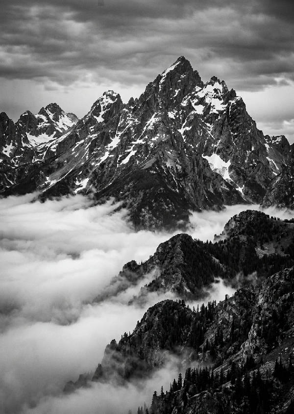 Detaljerat svartvitt fotografi av höga bergstoppar som sträcker sig mot himlen, dramatiskt ljus.