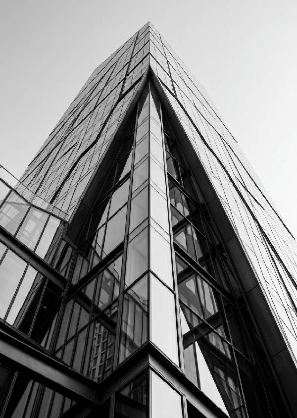 Vertikal svartvit arkitekturfotografi som visar en modern byggnad med rena linjer och skarpa kontraster i ett urbant landskap.