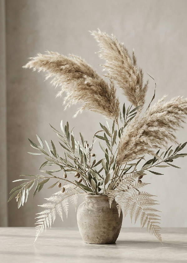 Närbild av ett mjukt, fotorealistiskt botaniskt stilleben med torkat pampasgräs, olivkvistar och ormbunkar i neutrala beigea och salviagröna toner upplysta av mjukt morgonljus.