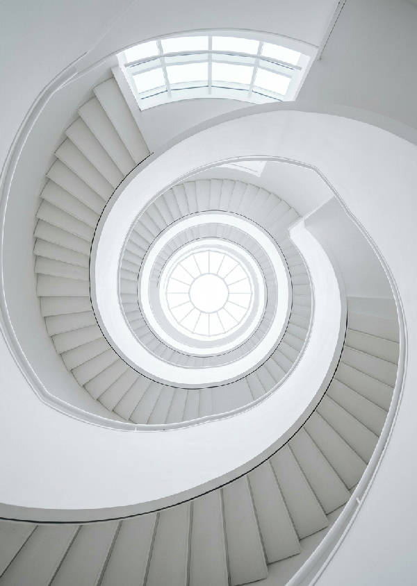Närbild av en modern vit spiraltrappa som elegant vrider sig uppåt med släta, minimalistiska räcken