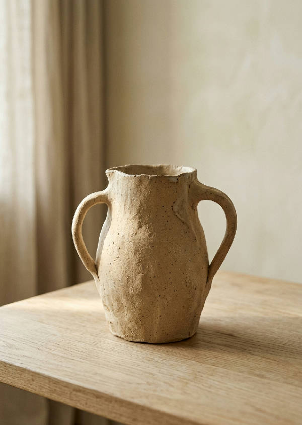 Enkel oregelbundet formad handgjord keramikvas i oglaserad matt sandbeige på ljust trä