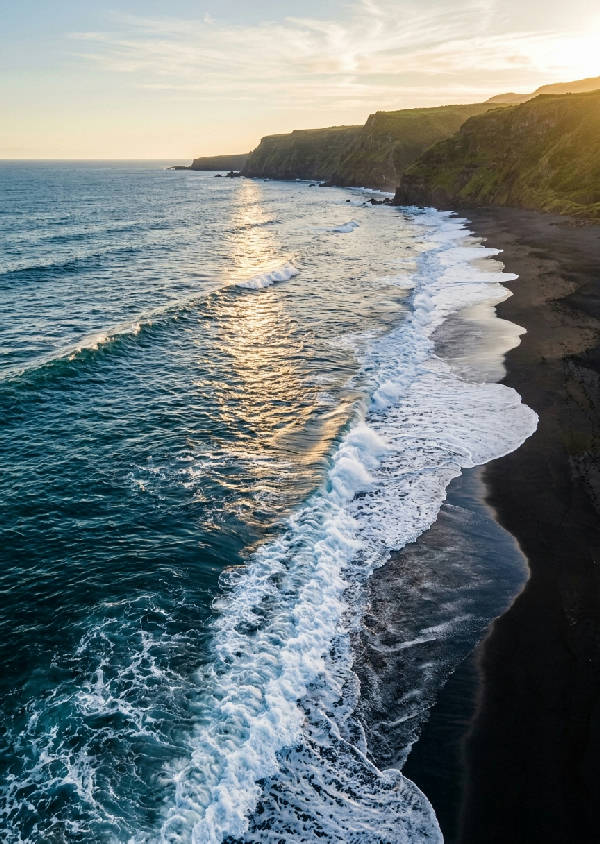 Flygfoto över en vacker kustlinje med turkost hav och gyllene sandstrand i porträttformat. Vågor slår mot land.