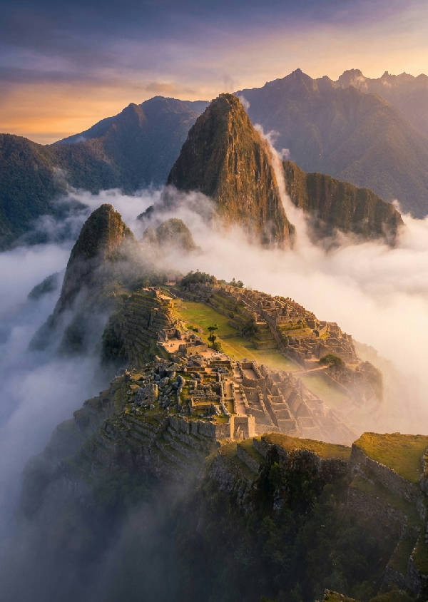 Hyperrealistisk flygbild av Machu Picchu vid soluppgången, med gyllene ljus som träffar terrasserna och omgivande berg som stiger upp ur dimman.
