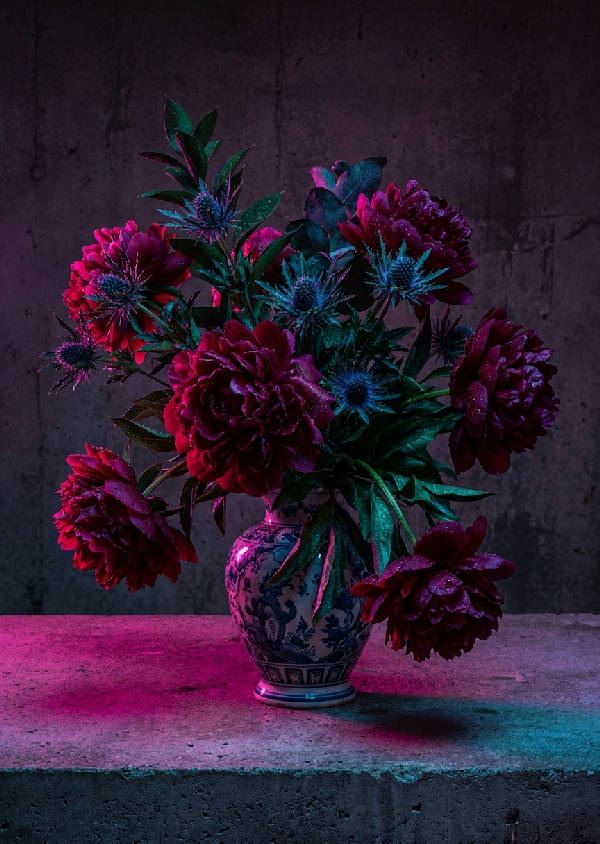 Porträttbild av en surrealistisk blomsterbukett i en keramisk vas, upplyst av neonrosa ljus som kastar dramatiska skuggor.