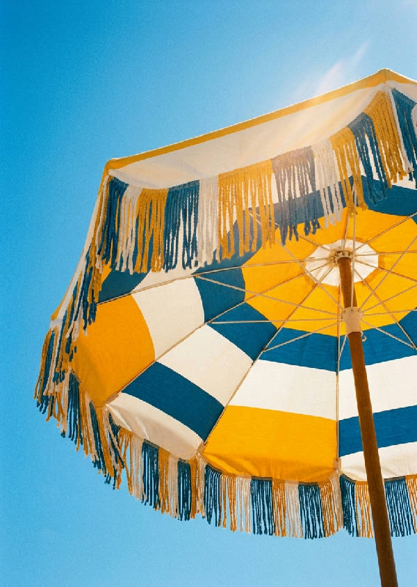 En vintage 1970-tals 35mm filmfotografi av ett retro, fransigt solparasoll i marigoldgult och vitt mot en klarblå sommarhimmel