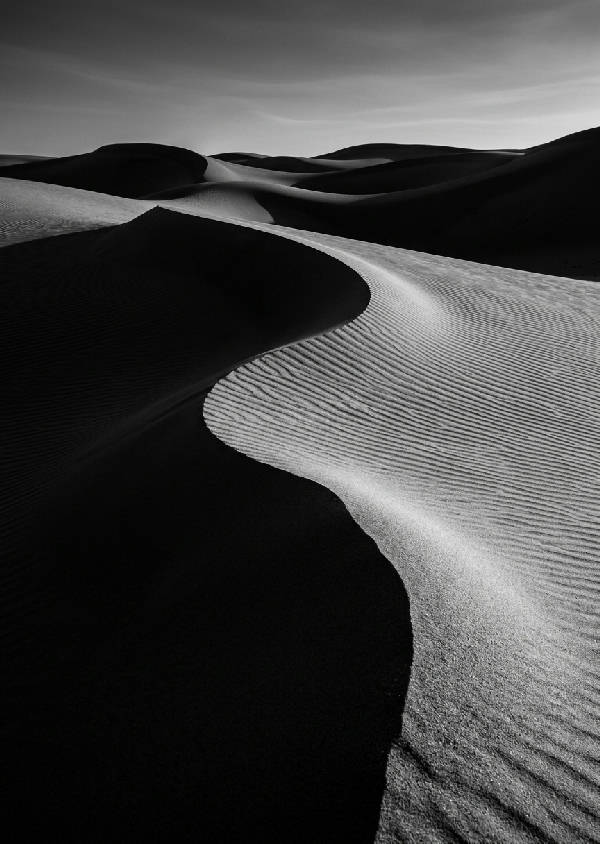 Abstrakt högkontrastfotografi av öknens sanddyner i djupt svarta och vita toner med dramatiska skuggor.
