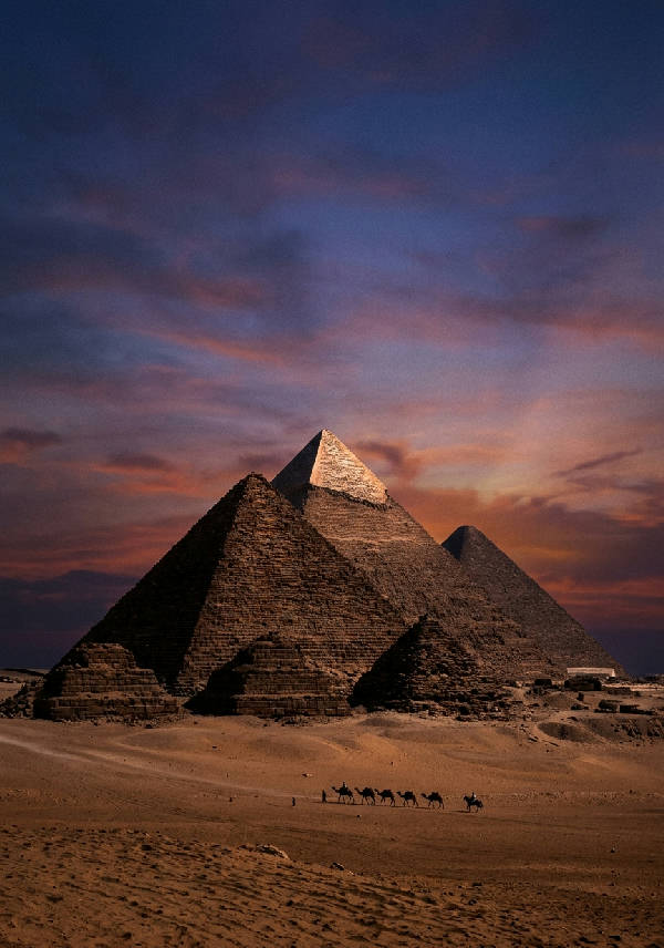 Ikonisk vertikal bild av pyramiderna i Giza i ett soldränkt ökenlandskap med en gul himmel.