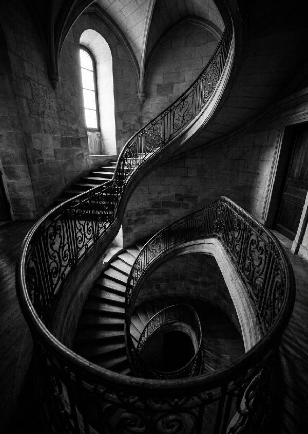 Dramatiskt svartvitt foto uppför en slingrande spiraltrappa i film noir stil med tydliga skuggor och arkitektoniska linjer.