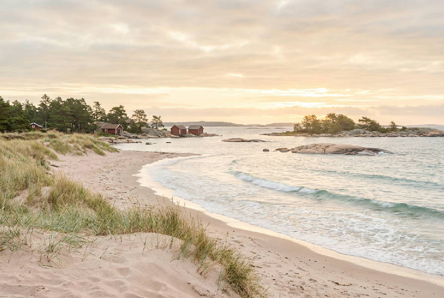 Fotorealistisk bild av en svensk sandstrand med mjukt vit sand och krämiga vågor som rullar in mot kusten under en klar himmel