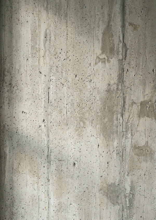 Närbild av en texturerad betongvägg med variationer i skugga och ljus, vilket framhäver materialets karaktär.