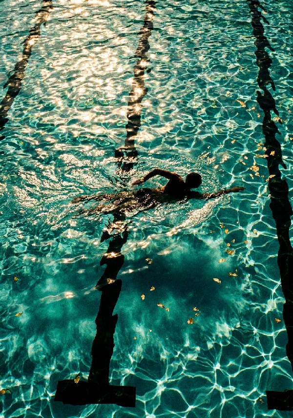 Flygfoto taget på 35mm film av en silhuett av en simmare som glider genom skimrande turkost poolvatten.