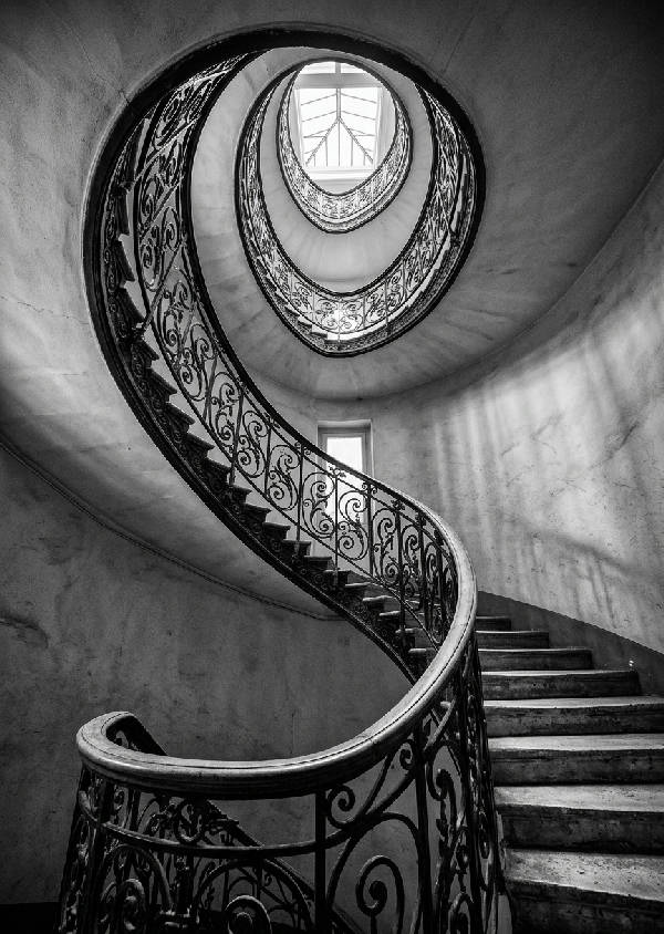 Svartvitt fotografi av en geometrisk spiraltrappa sedd underifrån som skapar ett hypnotiskt mönster.