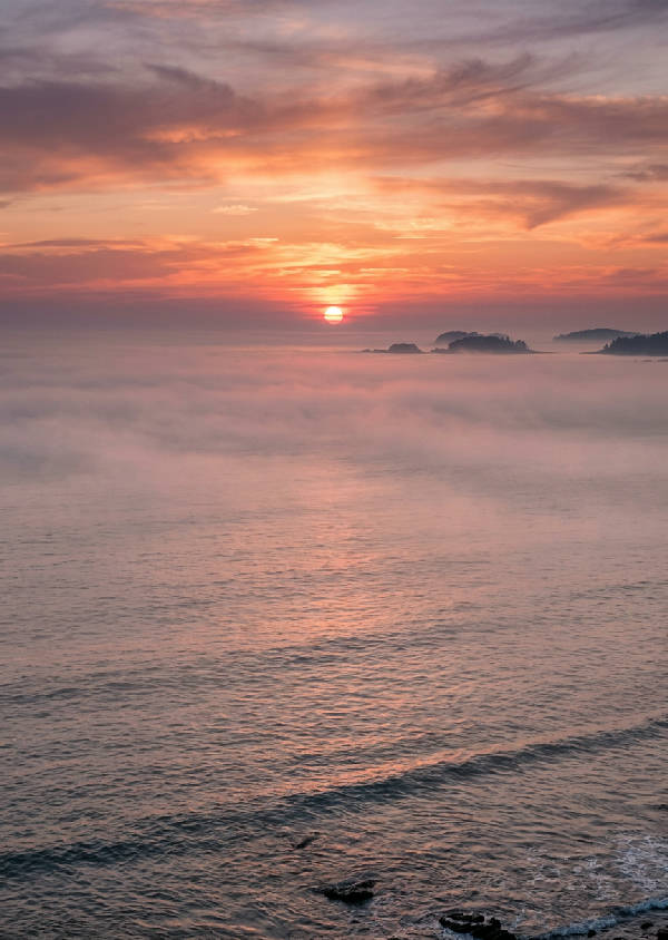 En rogivande bild av havet vid solnedgången, med en disig orange himmel som möter det lugna vattnet, vertikal