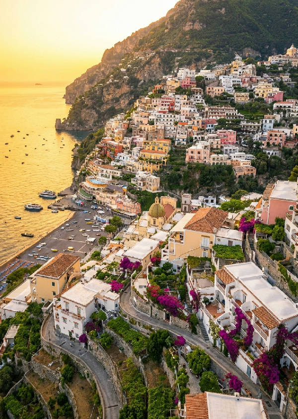 Detaljerad flygvy över Positano vid soluppgången, pastellfärgade hus på klippor, gyllene hav.