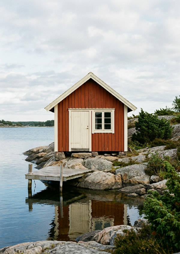Mjukfokuserad 35mm filmfotografi av ett ikoniskt rött båthus med vit trim på en granitstrandlinje